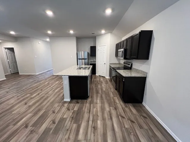 a living room with stainless steel appliances kitchen island granite countertop a sink dishwasher a stove and a refrigerator with wooden floor