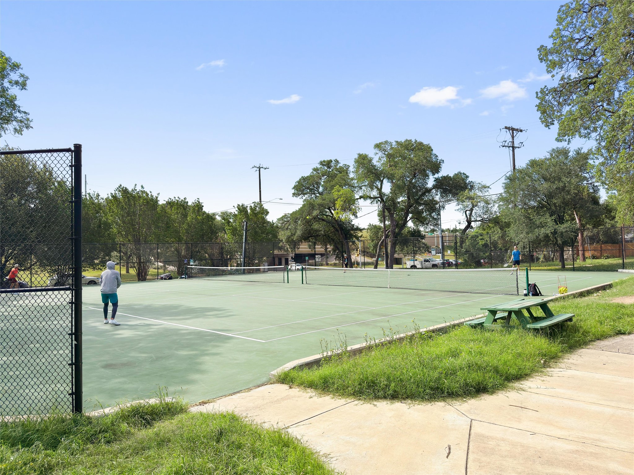 2208 Enfield Road, Unit 10500 Austin, TX 78703 - Photo 30 of 34 Tennis court with a green playing surface, surrounded by a chain-link fence and mature trees