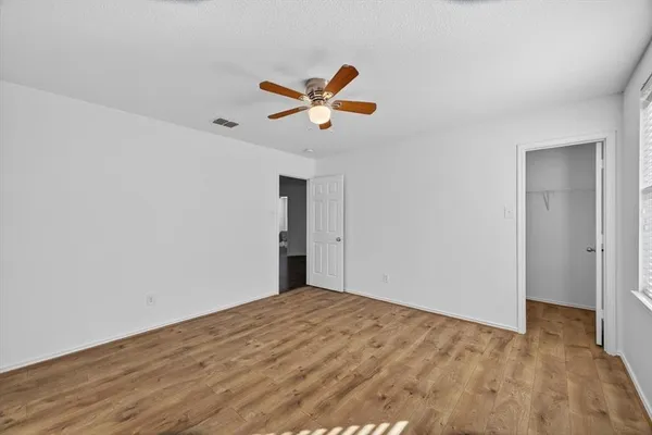 an empty room with wooden floor chandelier fan and windows
