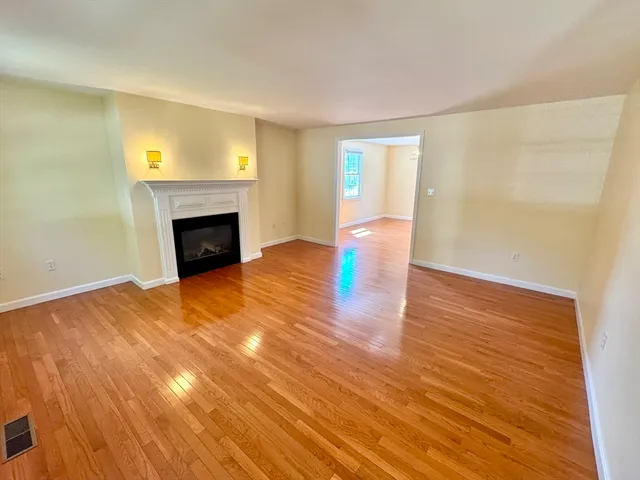 a view of an empty room with wooden floor and a fireplace
