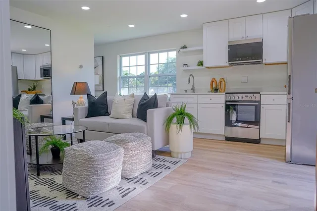a living room with stainless steel appliances furniture a flat screen tv and a kitchen view