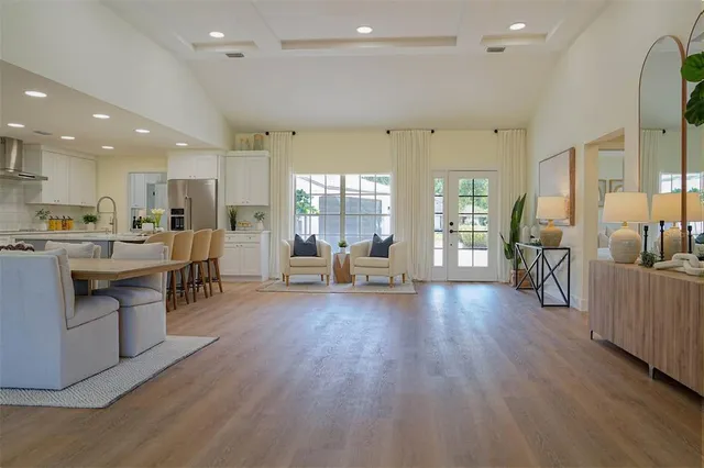 a living room with stainless steel appliances wooden floors and kitchen view