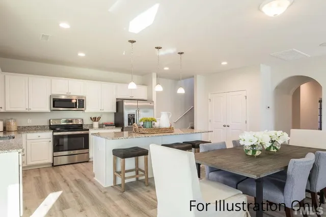 a kitchen with stainless steel appliances kitchen island granite countertop a stove a sink a refrigerator and white cabinets with wooden floor