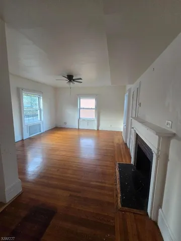 a view of an empty room with wooden floor fireplace and a window