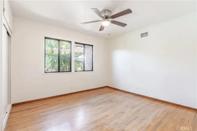 an empty room with wooden floor chandelier fan and windows