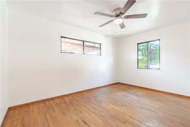 an empty room with wooden floor ceiling fan and windows