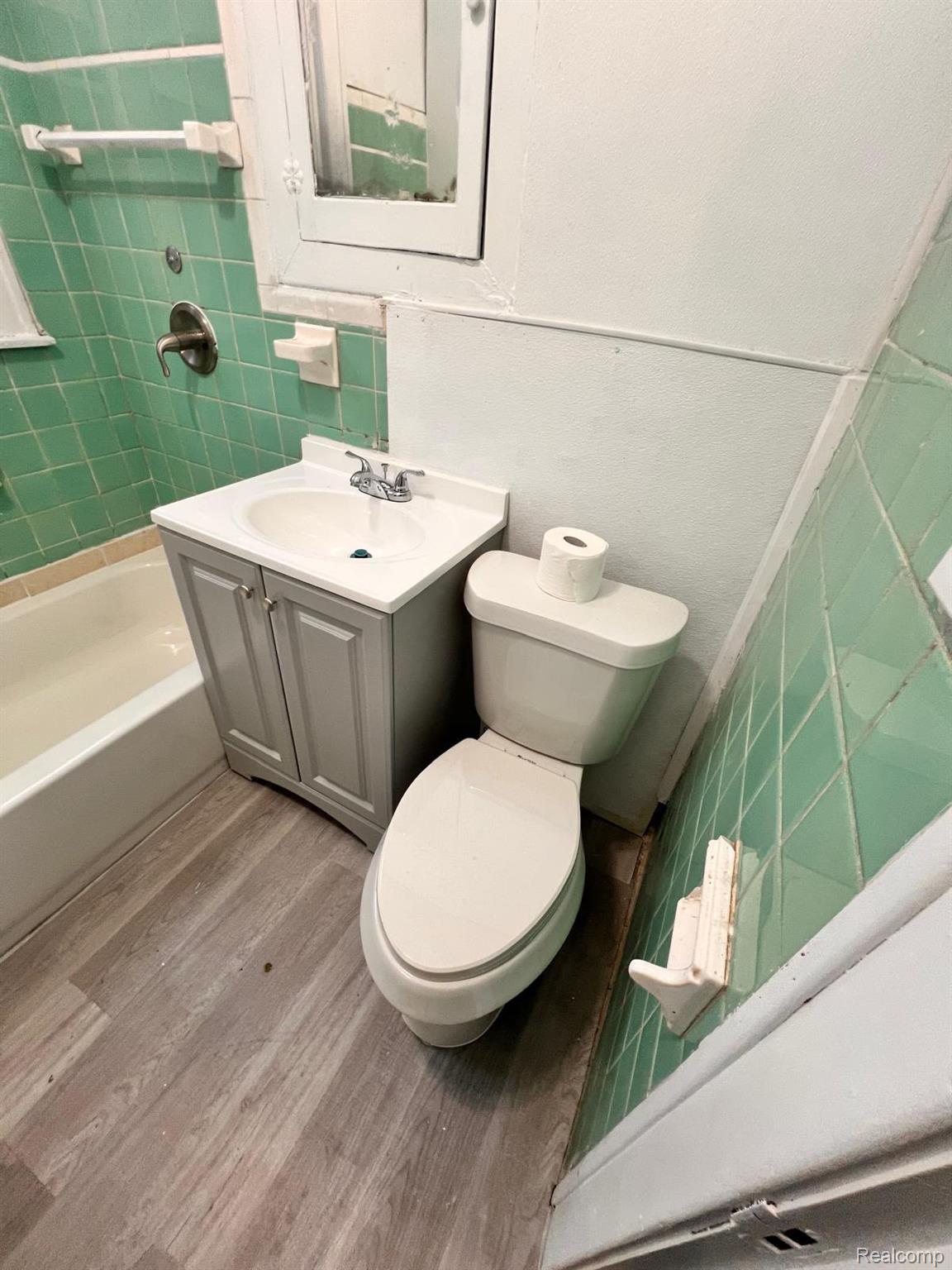 13768 Gable Street Hamtramck, MI 48212 - Photo 9 of 12 Bathroom featuring a white bathtub, green tiled shower surround, light gray vanity with a white sink, white toilet, and wood-finish flooring