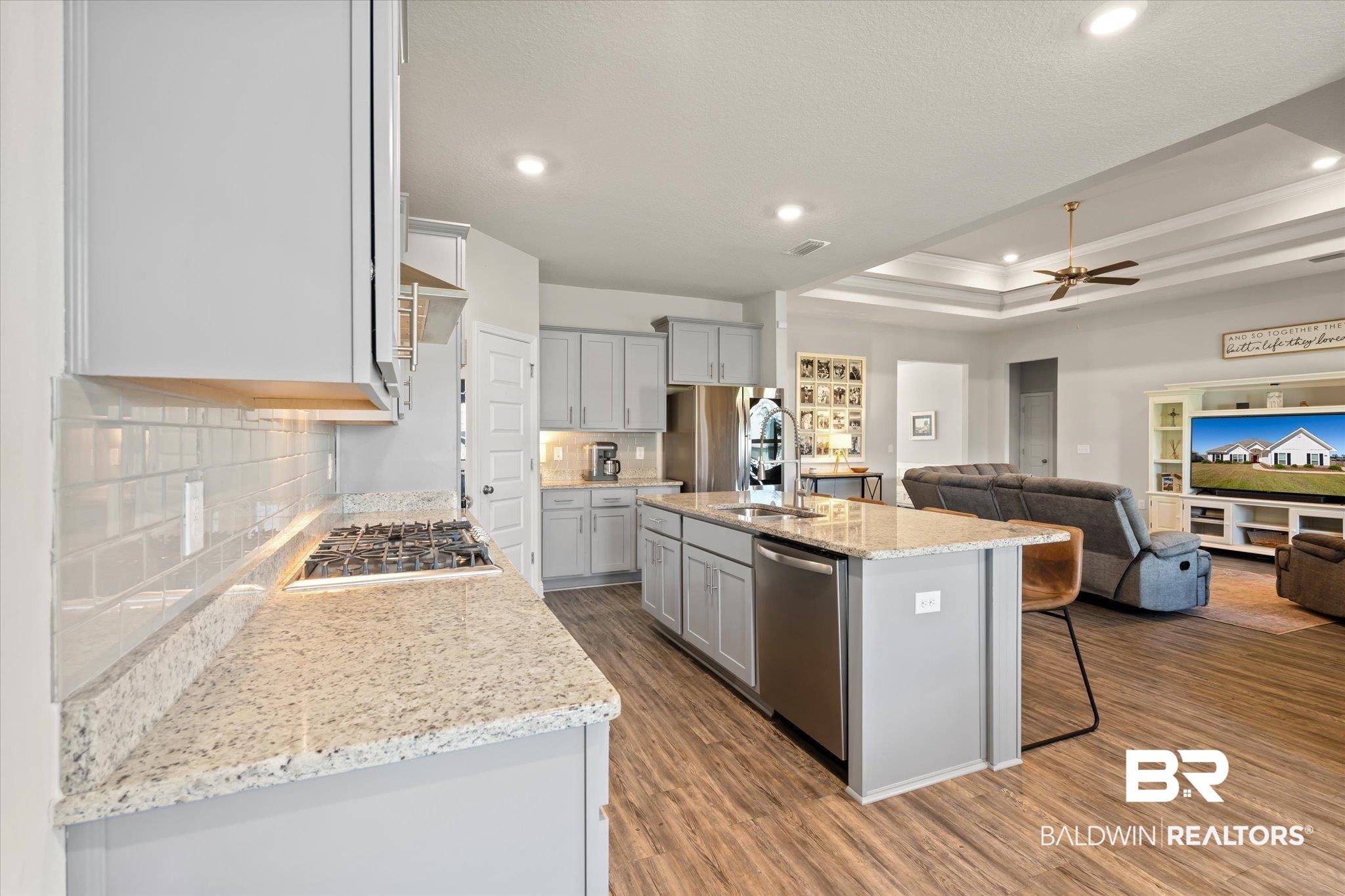 12899 Sanderling Loop Daphne, AL 36527 - Photo 10 of 28 Kitchen featuring tasteful backsplash, a center island with sink, a tray ceiling, light hardwood / wood-style flooring, and stainless steel appliances