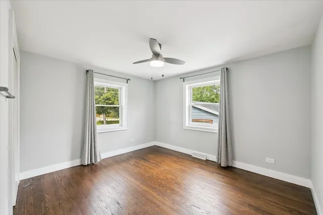 an empty room with wooden floor chandelier fan and windows