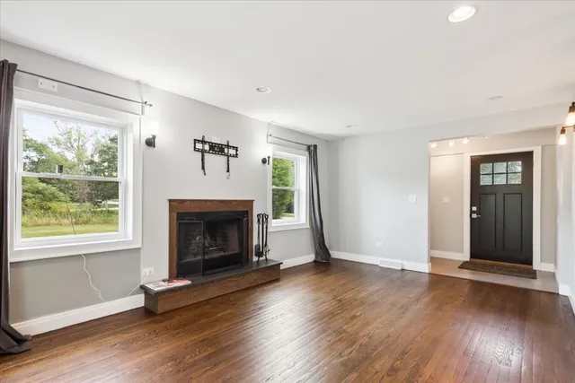 an empty room with wooden floor fireplace and windows
