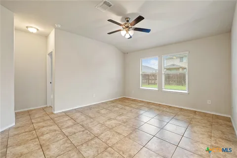 a view of an empty room and kitchen space with a ceiling fan