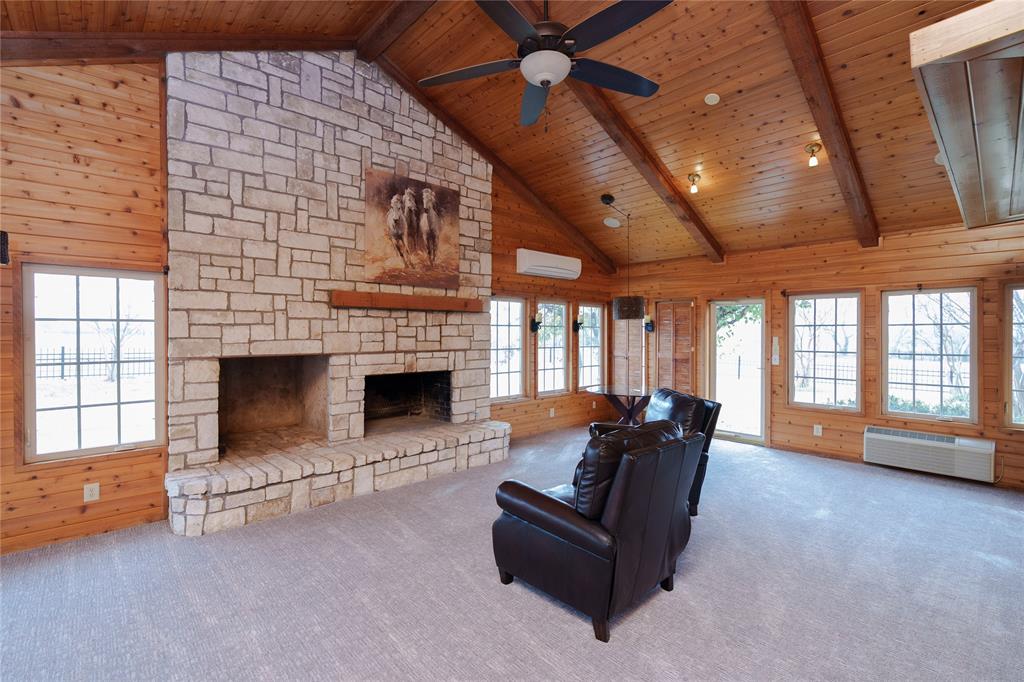 364 Parker Road, Unit A Van Alstyne, TX 75495 - Photo 18 of 39 Spacious room featuring a prominent stone fireplace with a raised hearth, vaulted wood-paneled ceiling with exposed beams, multiple grid-pattern windows, and a ceiling fan with integrated lighting