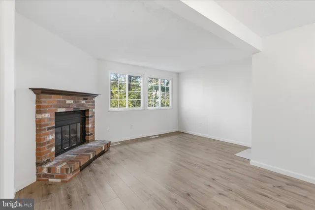 an empty room with wooden floor fireplace and windows