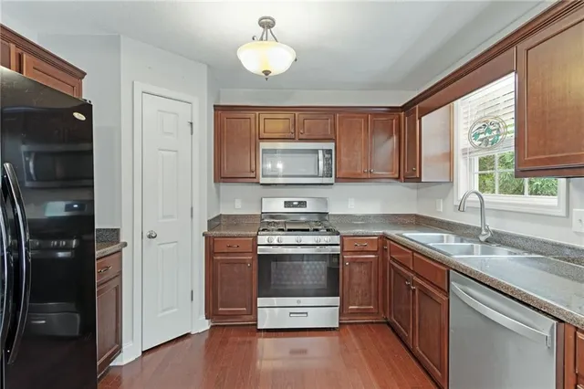 a kitchen with stainless steel appliances a refrigerator a sink dishwasher a dining table and chairs with wooden floor