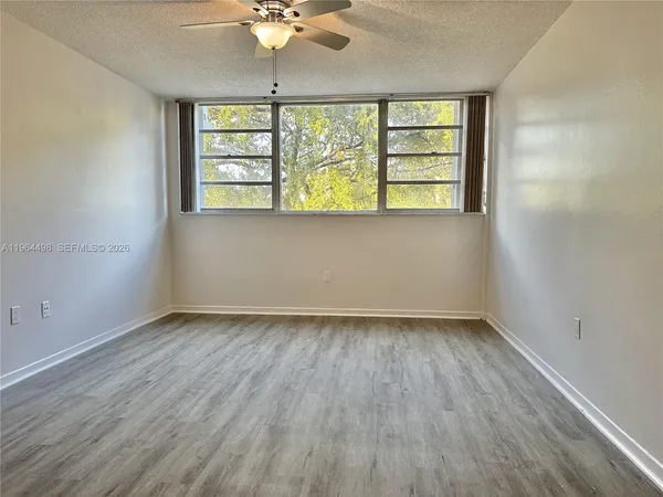 an empty room with wooden floor fan and windows