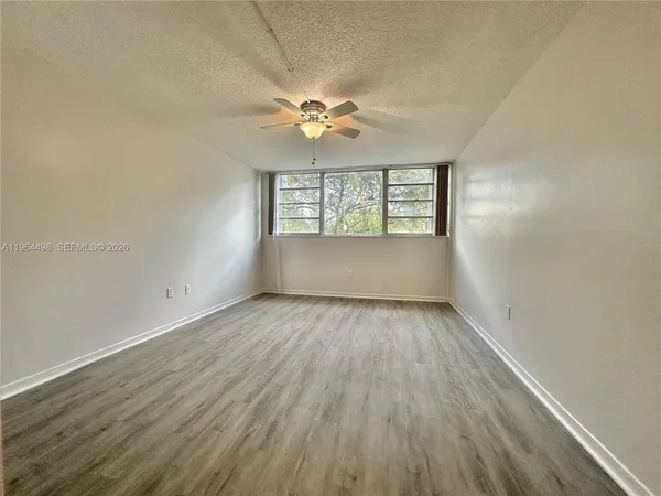 an empty room with wooden floor chandelier fan and windows