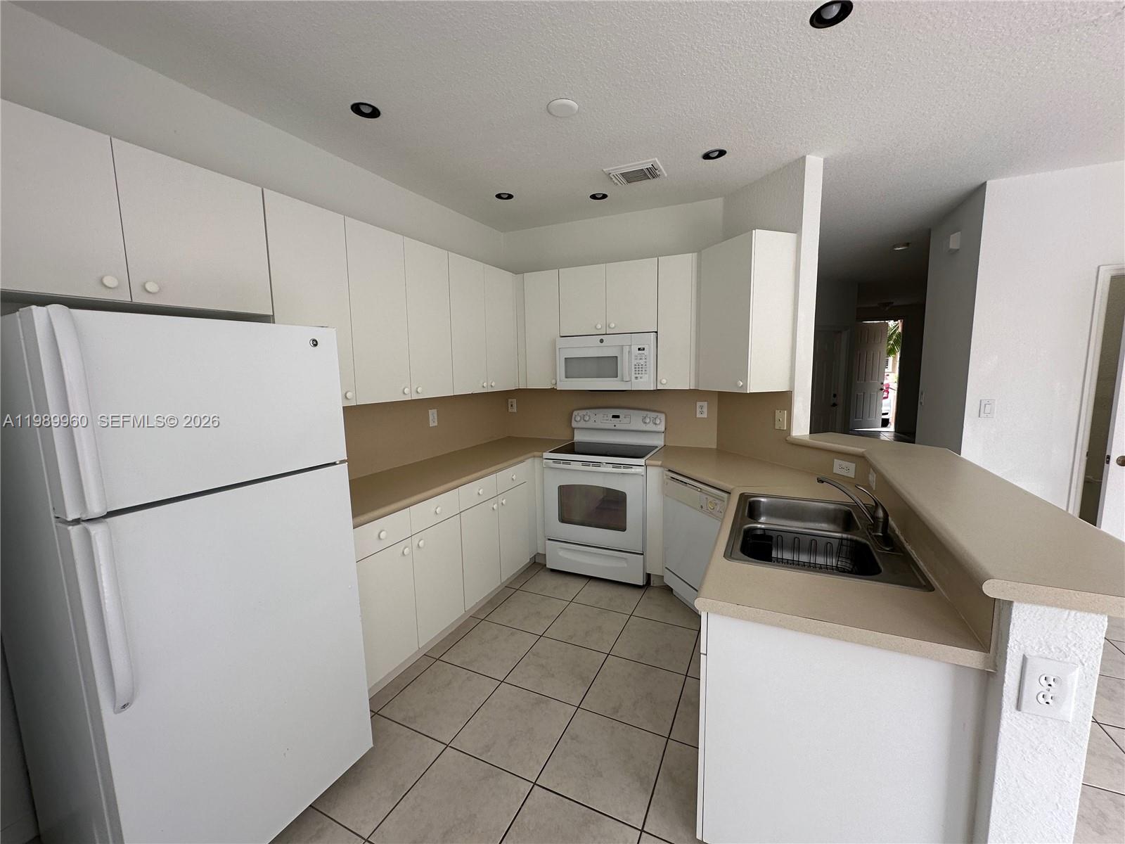 16602 Southwest 78th Terrace Miami, FL 33193 - Photo 16 of 18 a kitchen with a refrigerator a stove top oven and white cabinets