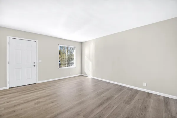 a view of an empty room with wooden floor and a window