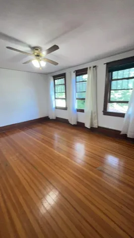 an empty room with wooden floor chandelier fan and windows