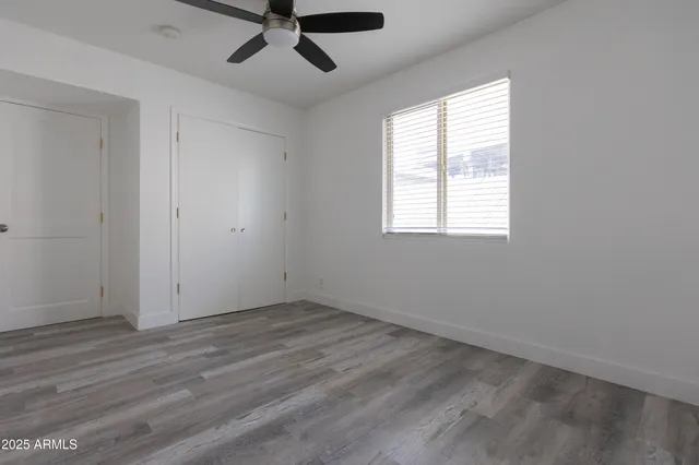 an empty room with wooden floor fan and windows
