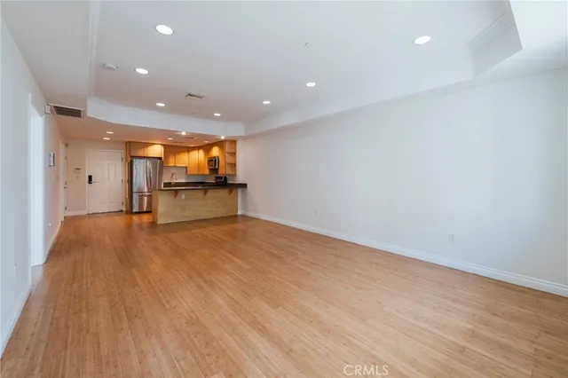 an empty room with wooden floor and a kitchen