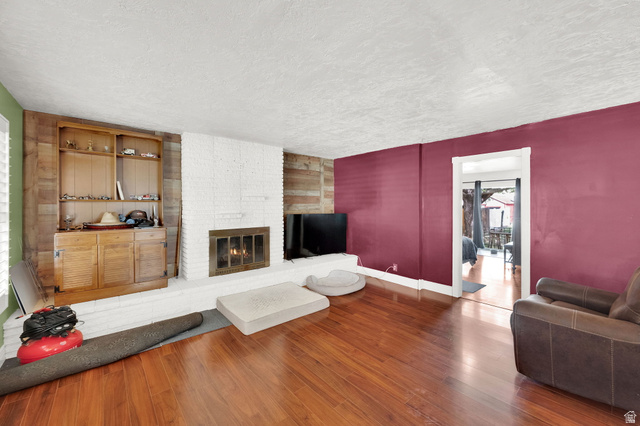 4635 Box Elder Street Murray, UT 84107 - Photo 4 of 21 Living area featuring wood-type flooring, a textured ceiling, and a brick fireplace