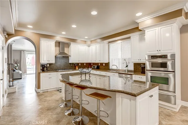 a kitchen with stainless steel appliances granite countertop a stove top oven a sink dishwasher a dining table and chairs with wooden floor