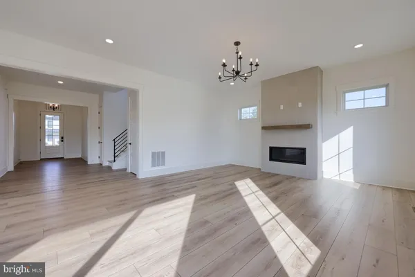 a view of an empty room with wooden floor and kitchen view