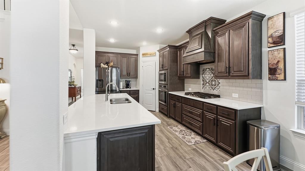 5216 Troupe Road McKinney, TX 75071 - Photo 9 of 40 Gourmet kitchen featuring a large central island with an undermount sink, dark wood-finish cabinetry, built-in stainless steel appliances, white countertops, and wood-finish flooring