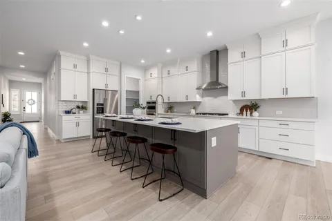 a kitchen with stainless steel appliances kitchen island granite countertop a stove a sink a refrigerator and white cabinets with wooden floor