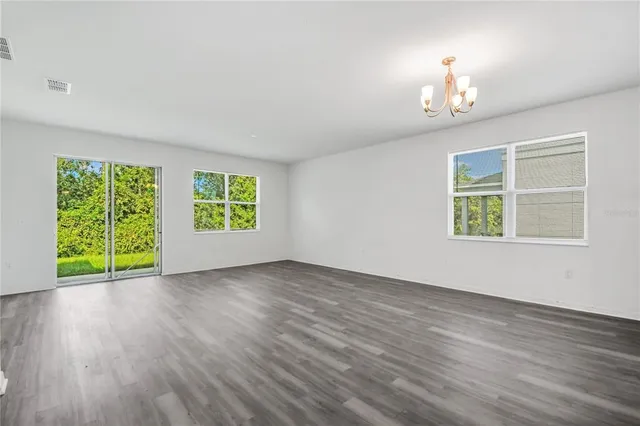 an empty room with wooden floor chandelier and windows