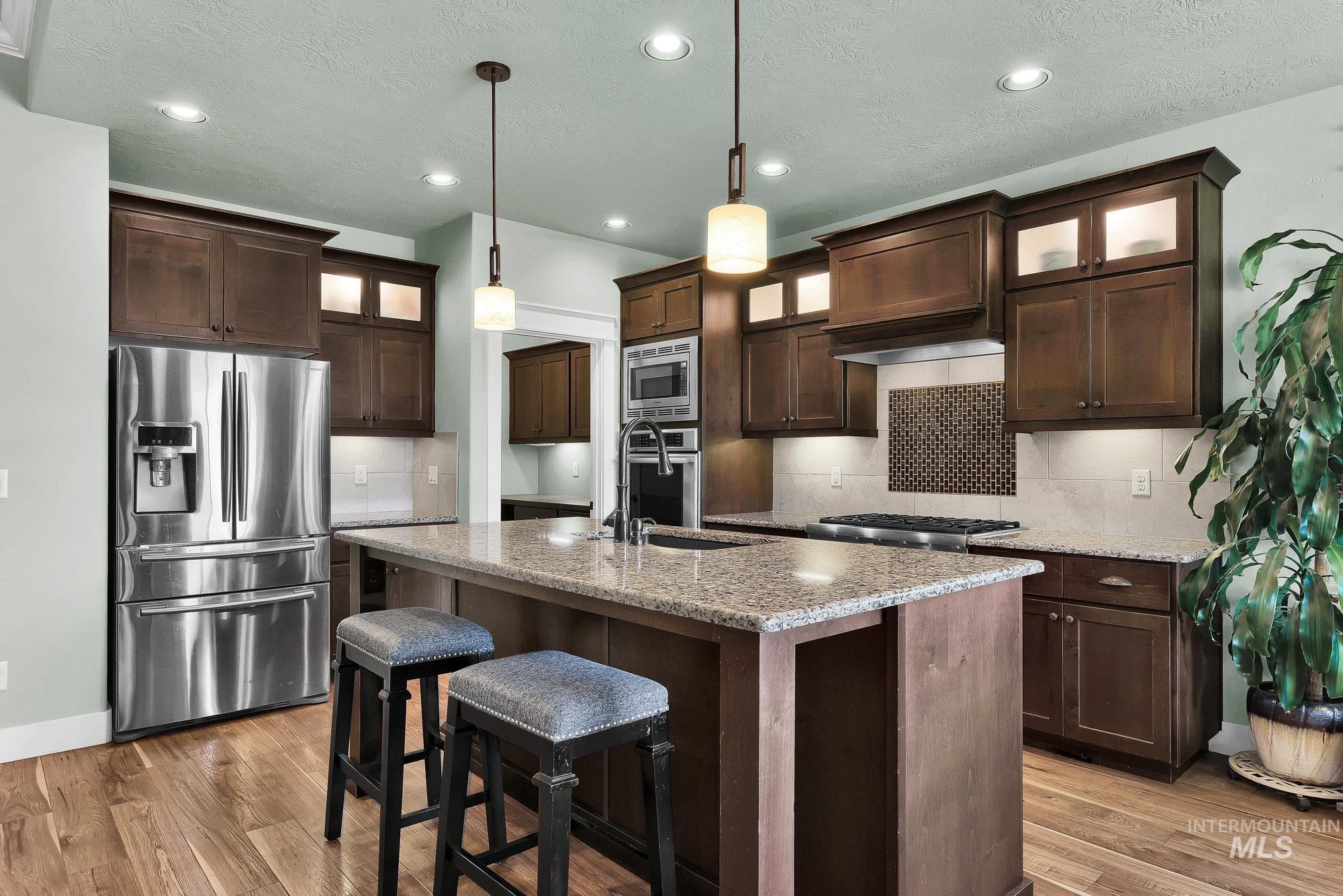 220 South Wildgrass Way Star, ID 83669 - Photo 10 of 50 Kitchen with wood flooring, dark wood cabinetry, stainless steel double ovens, and a center island with a stone countertop