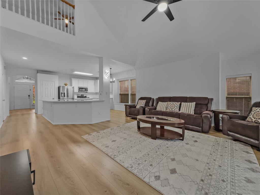 3008 Devlin Ridge Drive Plano, TX 75025 - Photo 10 of 24 Open concept living area featuring wood-finish flooring, a kitchen island with seating, stainless steel appliances, a ceiling fan, and a second-story overlook with a white railing