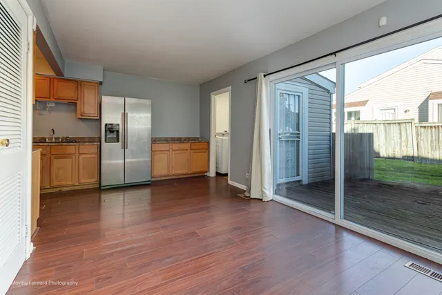an empty room with wooden floor kitchen view and windows