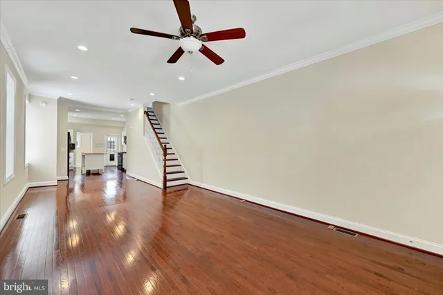 a view of an empty room with wooden floor ceiling fan