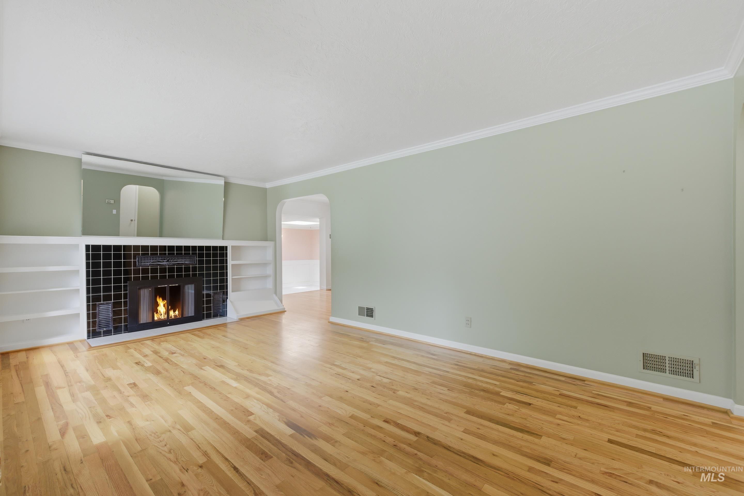 504 West Howe Street Boise, ID 83706 - Photo 6 of 47 Living area featuring light wood-finish flooring, a fireplace with black tile surround, built-in shelving, white crown molding, and an arched doorway