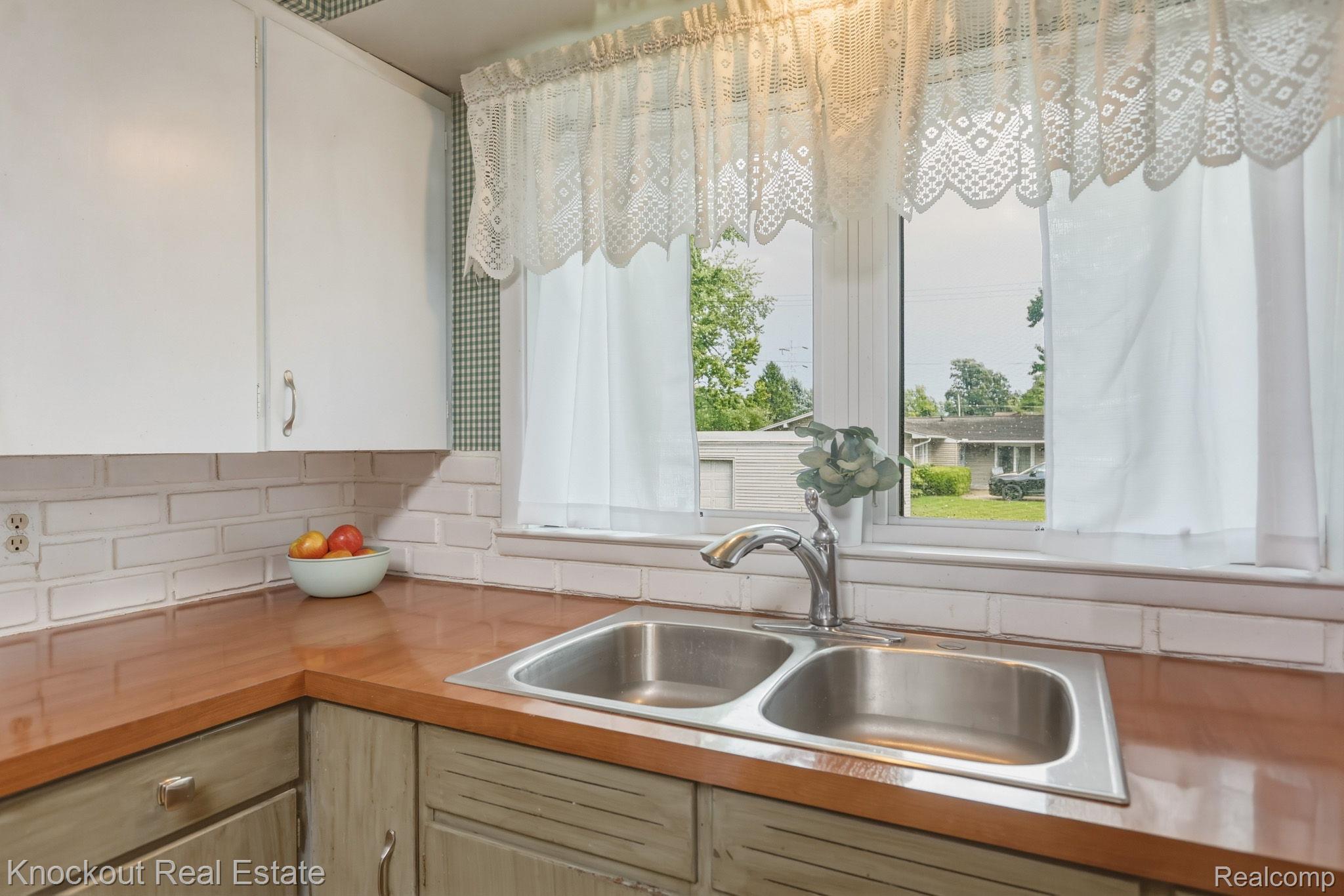 1755 South Reese Road Reese, MI 48757 - Photo 16 of 69 Dual basin stainless steel sink with a chrome faucet, wood-finish countertops, white painted upper cabinetry, and a white brick-style backsplash