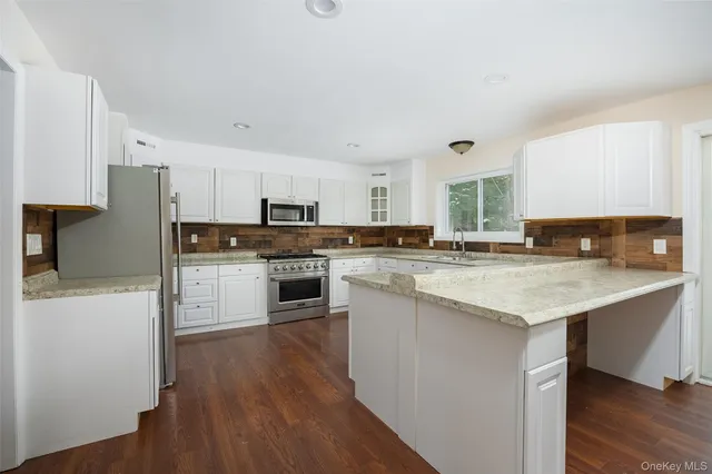 a kitchen with stainless steel appliances kitchen island granite countertop a stove a sink a refrigerator and white cabinets with wooden floor