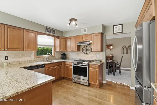 a kitchen with stainless steel appliances granite countertop hardwood floor sink stove dining table and chairs