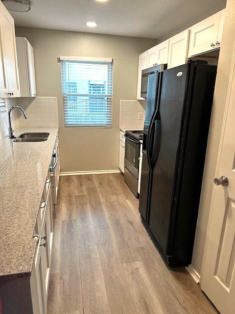 371 Fantail Loop, Unit B Austin, TX 78734 - Photo 3 of 10 Kitchen featuring white cabinetry, black appliances, light wood-style floors, light stone counters, and recessed lighting