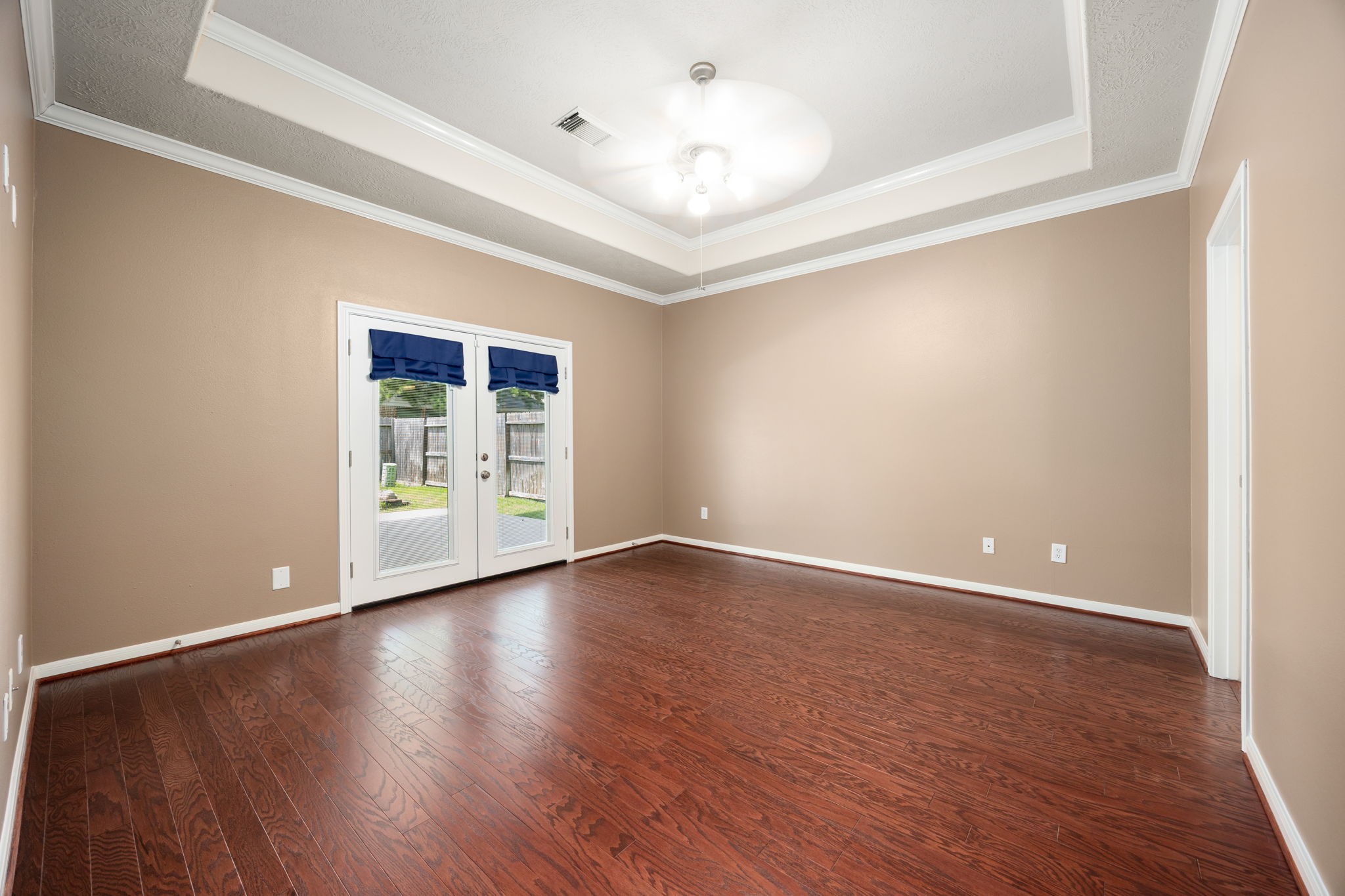 4526 Countrypines Drive Spring, TX 77388 - Photo 22 of 38 Retreat to this spacious primary suite featuring beautiful tray ceilings accented by elegant crown molding. Rich wood-look plank flooring adds warmth, while double French doors open directly to the backyard for a private morning coffee spot.
