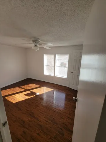 an empty room with wooden floor fan and windows
