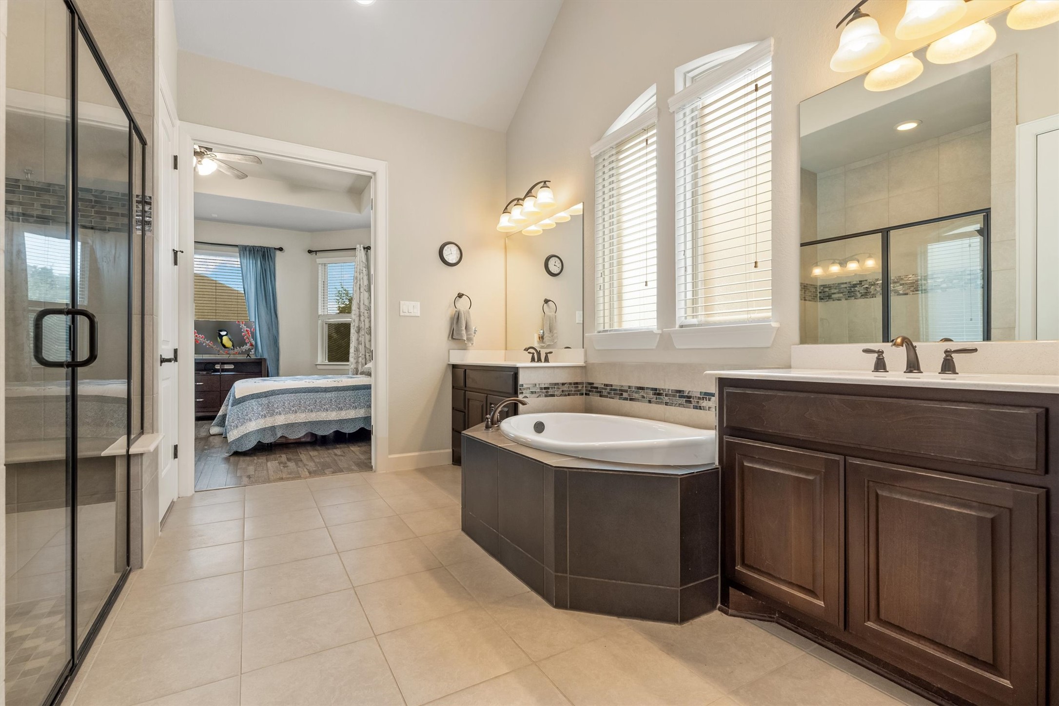 1004 Hezekiah Lane Leander, TX 78641 - Photo 20 of 36 Spacious bathroom featuring a glass-enclosed shower with tiled bench, a corner soaking tub, dual vanity sinks, and arched windows with blinds