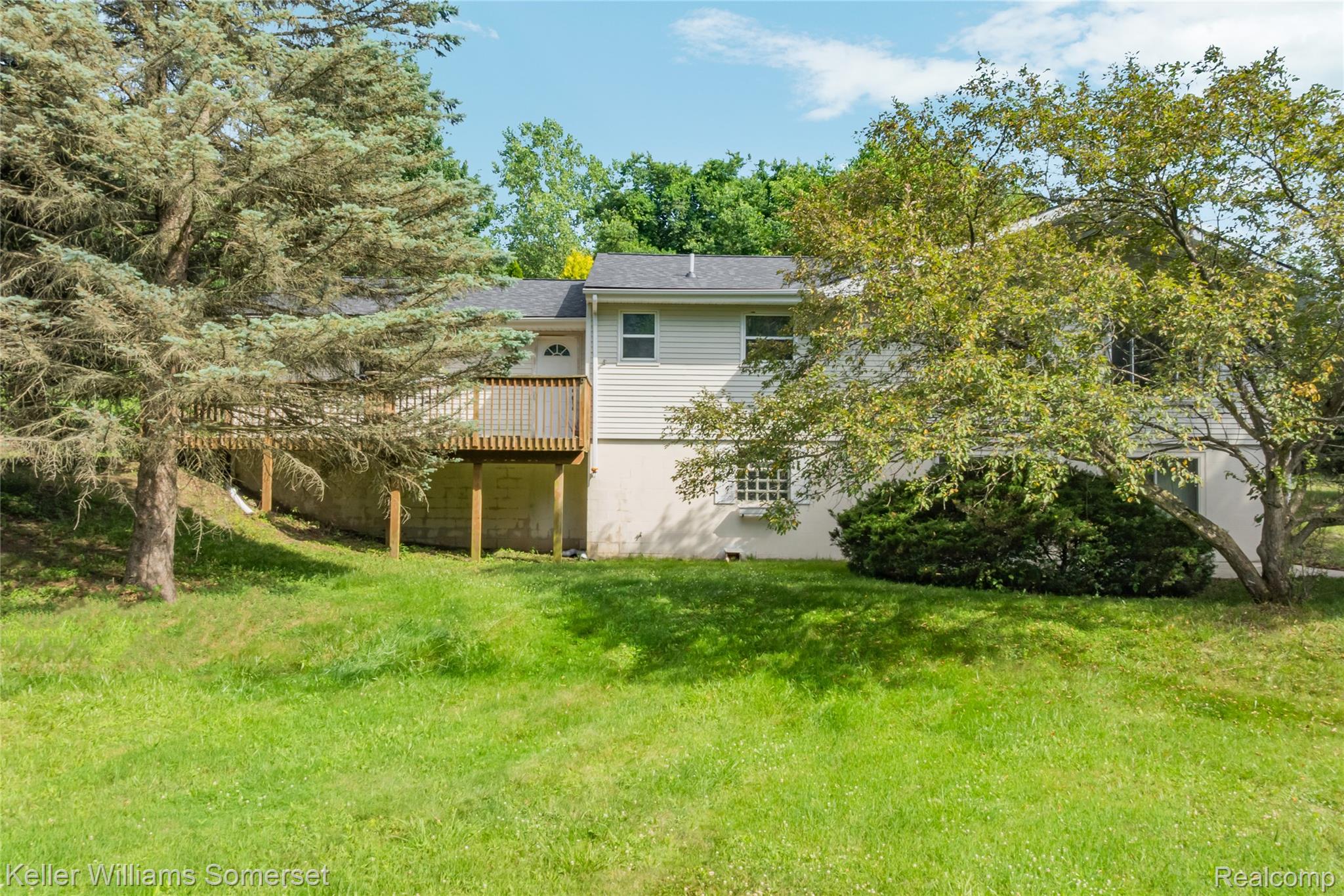 2344 Rochester Road Leonard, MI 48367 - Photo 56 of 66 Rear exterior featuring light-colored siding, a wooden deck with railing, and a sloped grassy yard