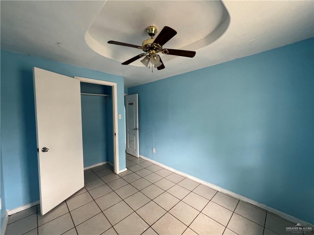1015 Martinez Street Weslaco, TX 78596 - Photo 9 of 10 Unfurnished bedroom with a ceiling fan, a closet, a tray ceiling, and light tile patterned floors
