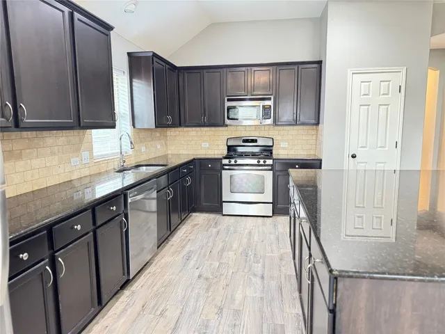 a kitchen with stainless steel appliances granite countertop wooden cabinets a sink dishwasher a stove and a refrigerator with wooden floor