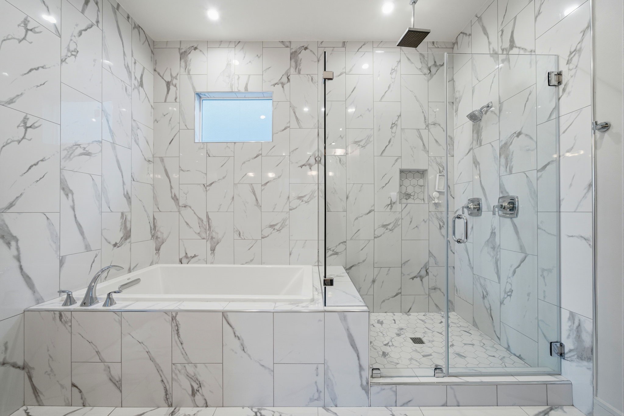 1405 Vermont Street, Unit A Houston, TX 77006 - Photo 30 of 46 Renovated primary ensuite bath features a seamless glass-enclosed shower and a separate soaking tub framed by floor-to-ceiling porcelain tile. Designer finishes like the rainfall showerhead and sleek chrome fixtures elevate this spa-inspired sanctuary, while a transom window provides a touch of natural light.