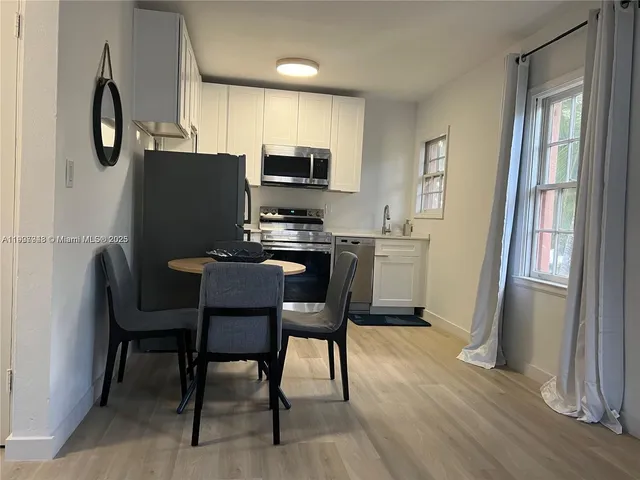 a kitchen with stainless steel appliances a dining table chairs refrigerator and microwave