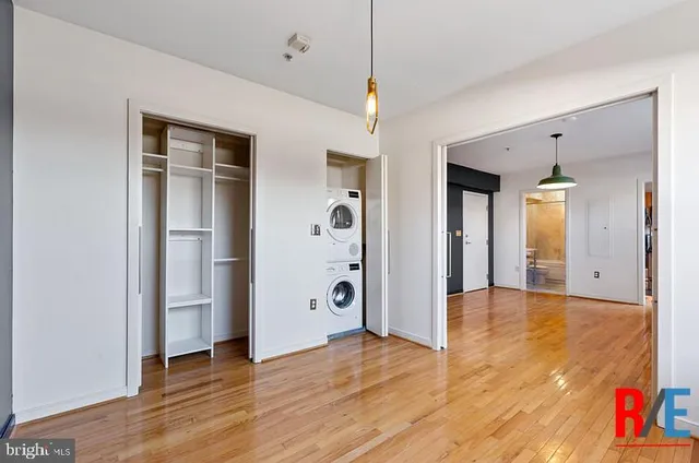 a view of an empty room with wooden floor and a kitchen