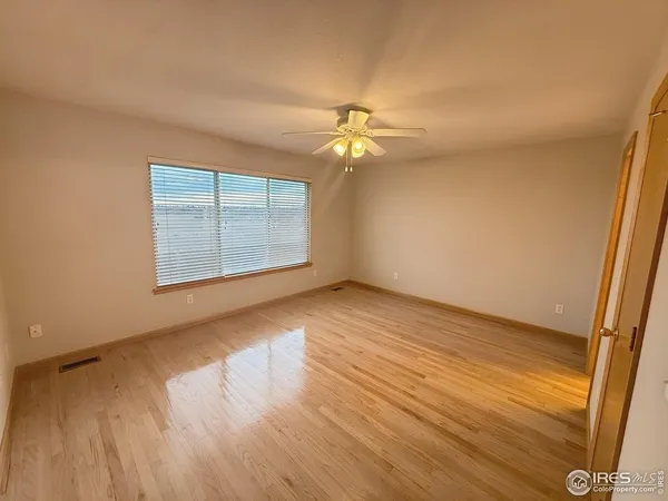 an empty room with wooden floor chandelier fan and windows